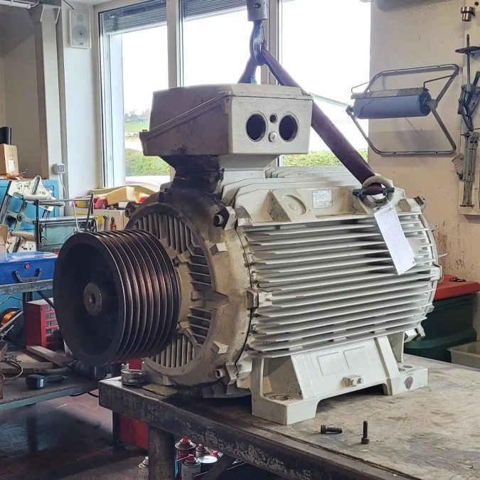 Großer Elektromotor mit Riemenscheibe steht auf einer Werkbank in einer Werkstatt.