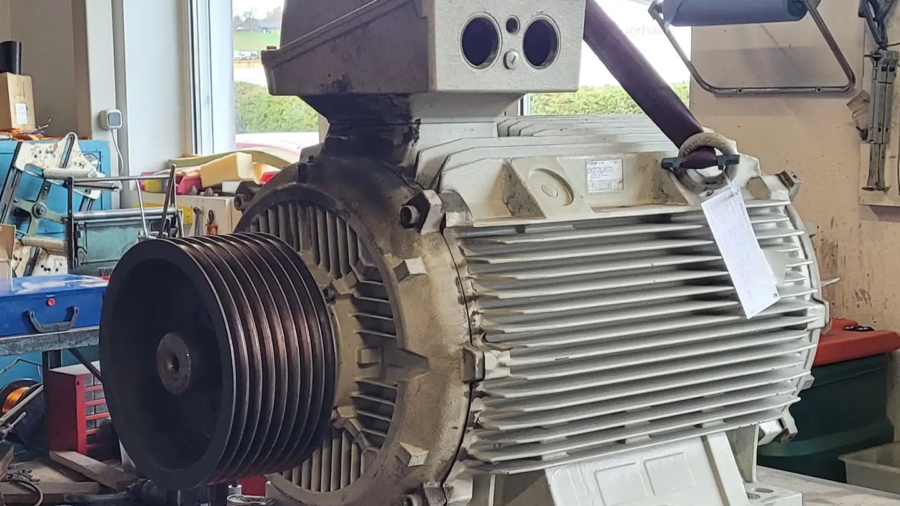 Großer Elektromotor mit Riemenscheibe steht auf einer Werkbank in einer Werkstatt.