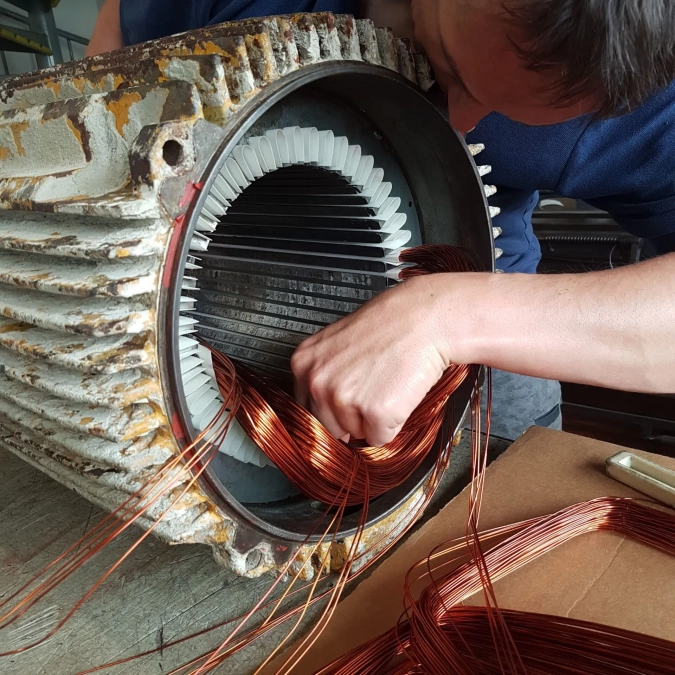 Nahaufnahme: Kupferdraht wird in den Stator eines Elektromotors eingefädelt (Motor wickeln).