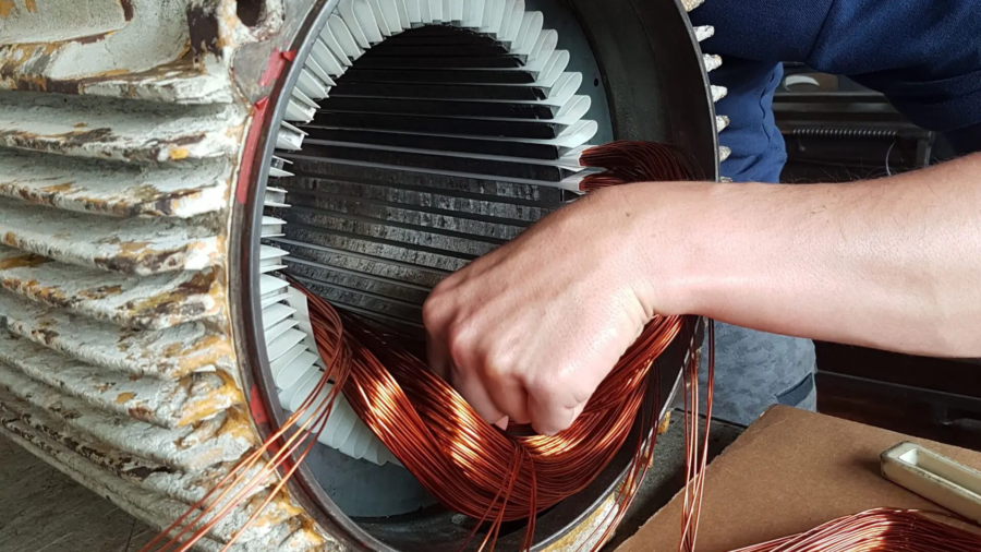 Nahaufnahme: Kupferdraht wird in den Stator eines Elektromotors eingefädelt (Motor wickeln).