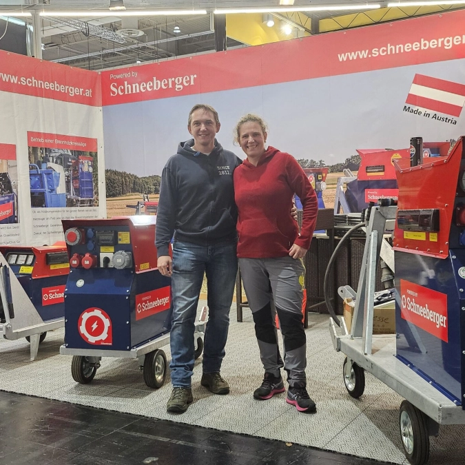Zwei Personen stehen auf einem Messestand vor Schneeberger Geräten und Branding.
