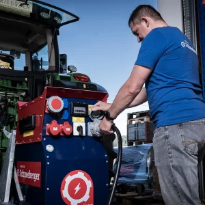 Ein Mitarbeiter schließt in der Werkshalle ein Kabel an einen Schneeberger Zapfwellengenerator am Traktor an.