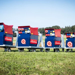 Vier Schneeberger Zapfwellengeneratoren in unterschiedlichen Größen stehen auf einer Wiese vor Feldern.